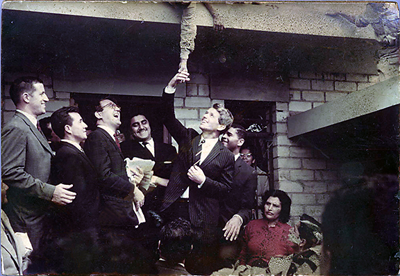 Sen. Robert Kennedy (surrounded by Peace Corps staff as well as American and Peruvian officials) reaches up to shake the hand of a young man in the slum of Comas, Peru, during a tour of impoverished communities in Latin America. This is the first publication of the Nov. 12, 1965, photograph taken by then-Peace Corps Volunteer Thomas Pleasure