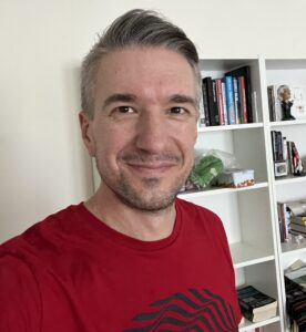 A headshot image of Greg Emerson with a bookshelf in the background